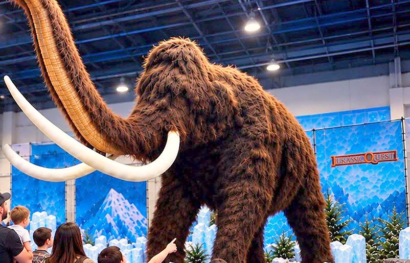 A towering woolly mammoth with kids looking up